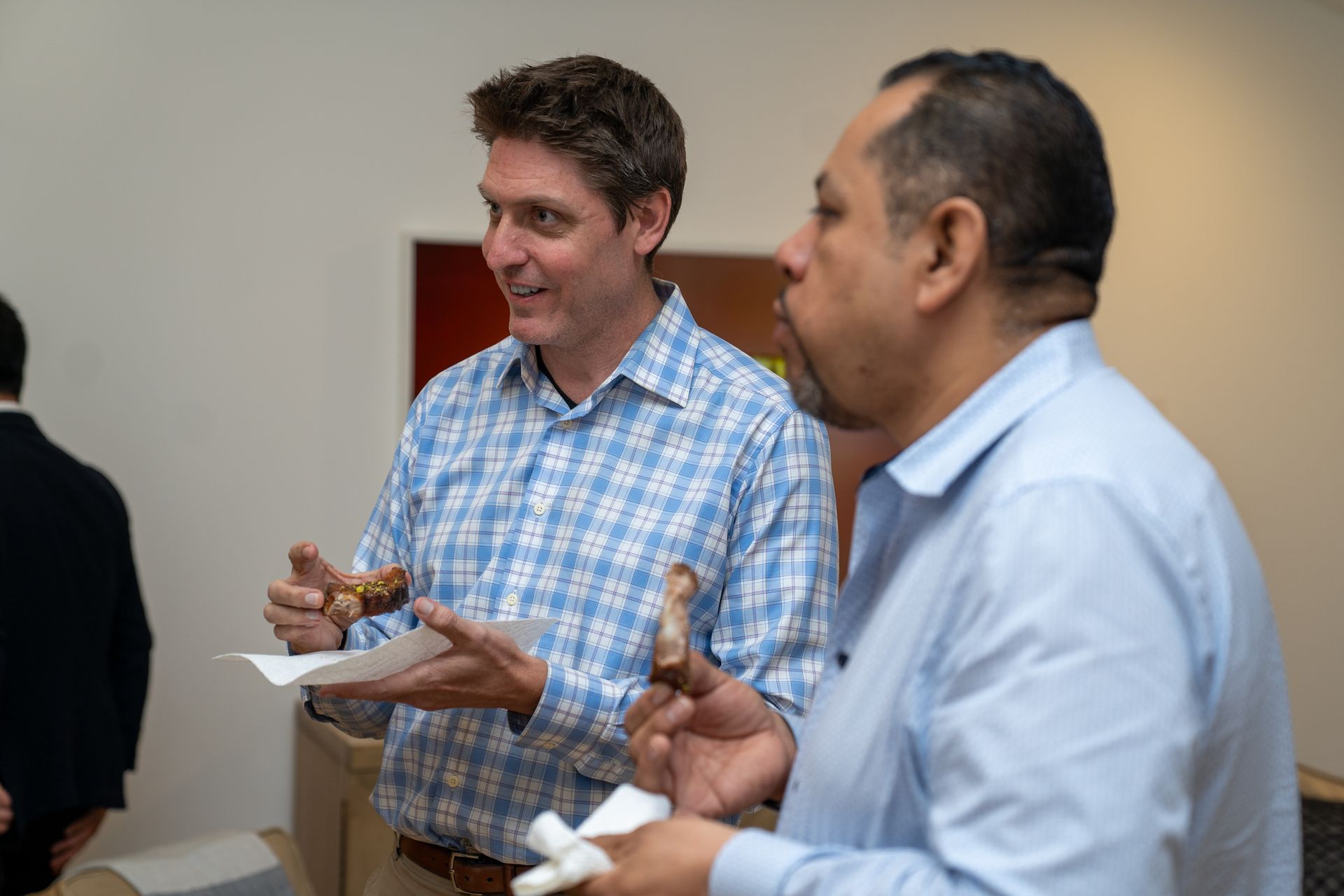 Two men are standing next to each other eating food.