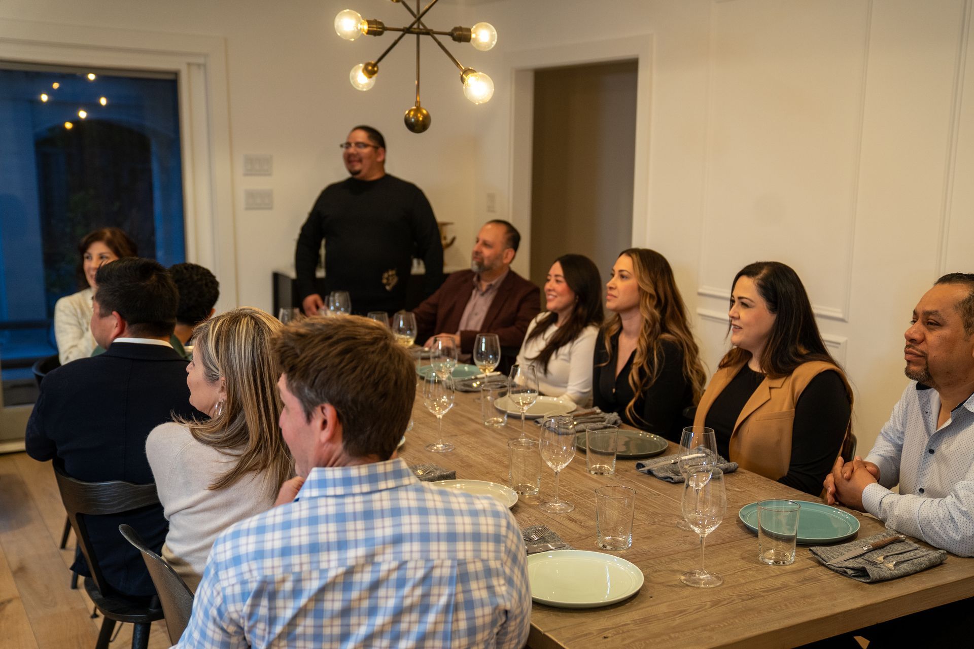 A group of people are sitting at a long table with plates and glasses of wine.