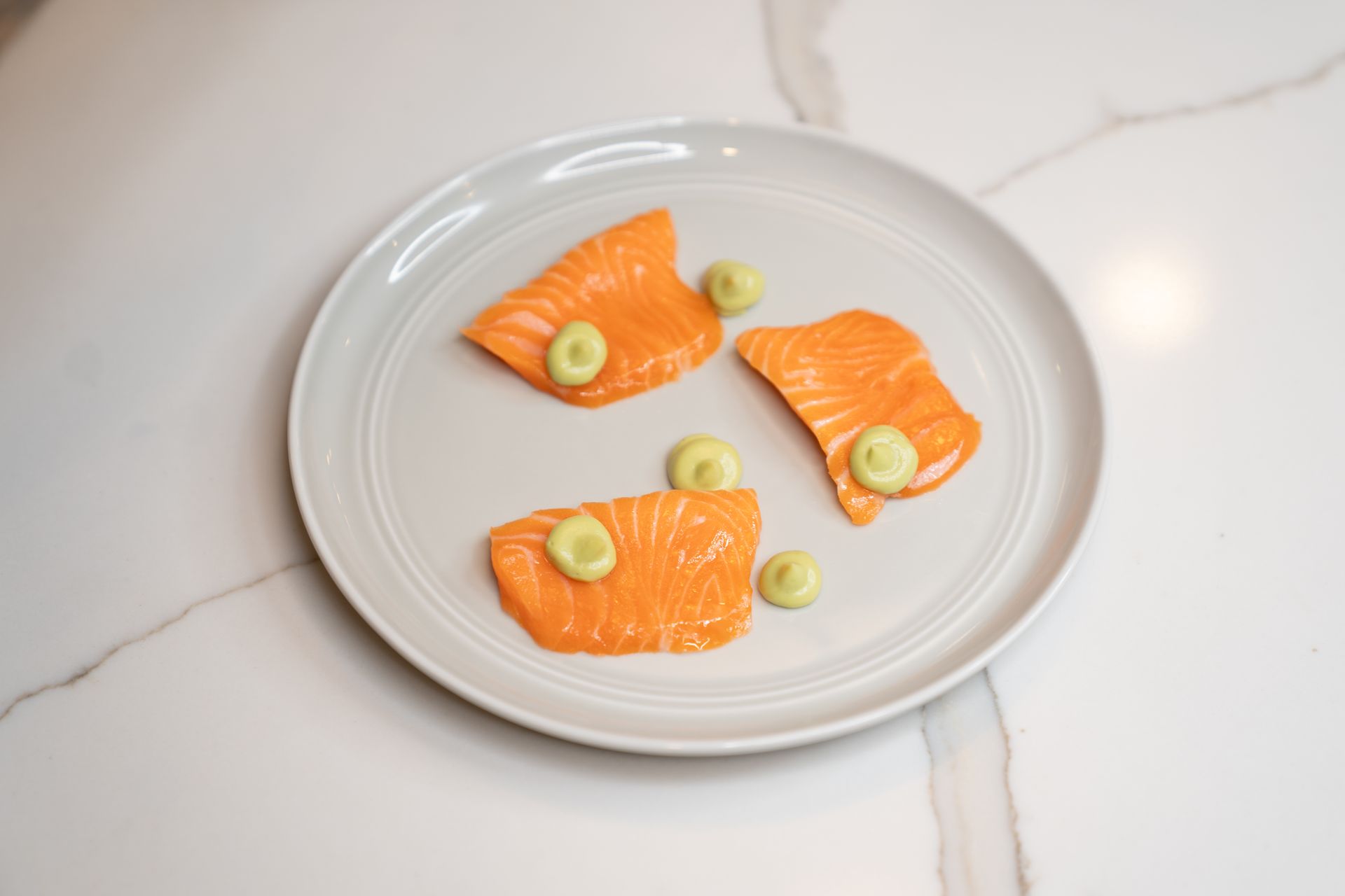 A white plate topped with slices of salmon and green onions.