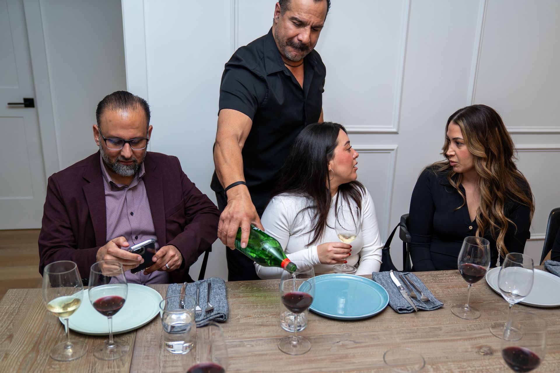 A man is pouring wine into a woman 's glass at a dinner table.