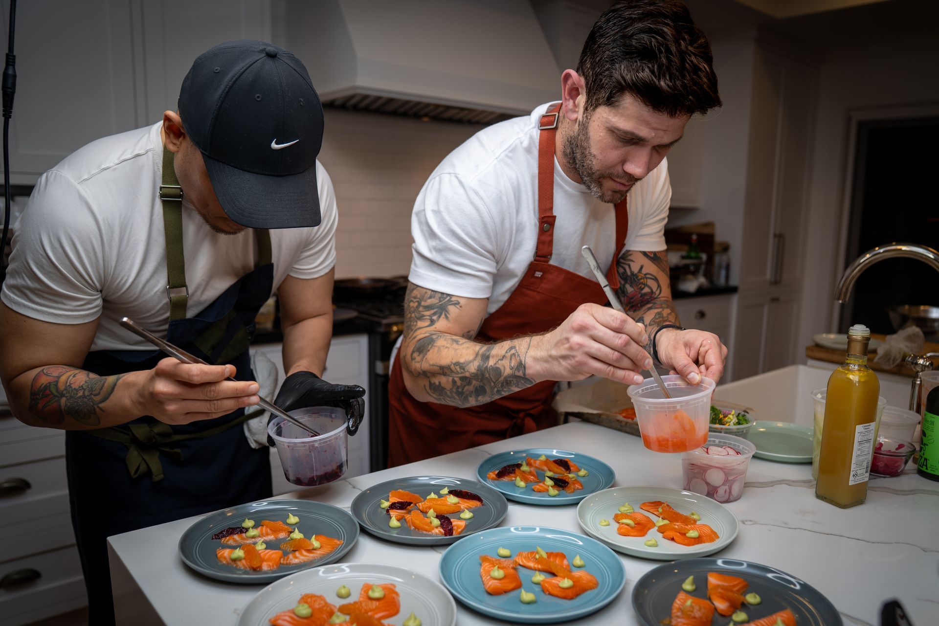 Two men are preparing food on plates in a kitchen.