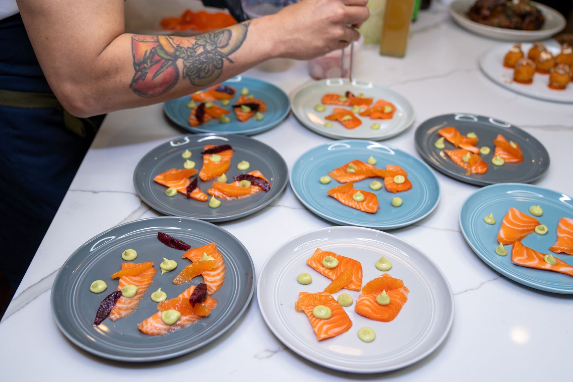 A person with a tattoo on their arm is preparing plates of food on a table.