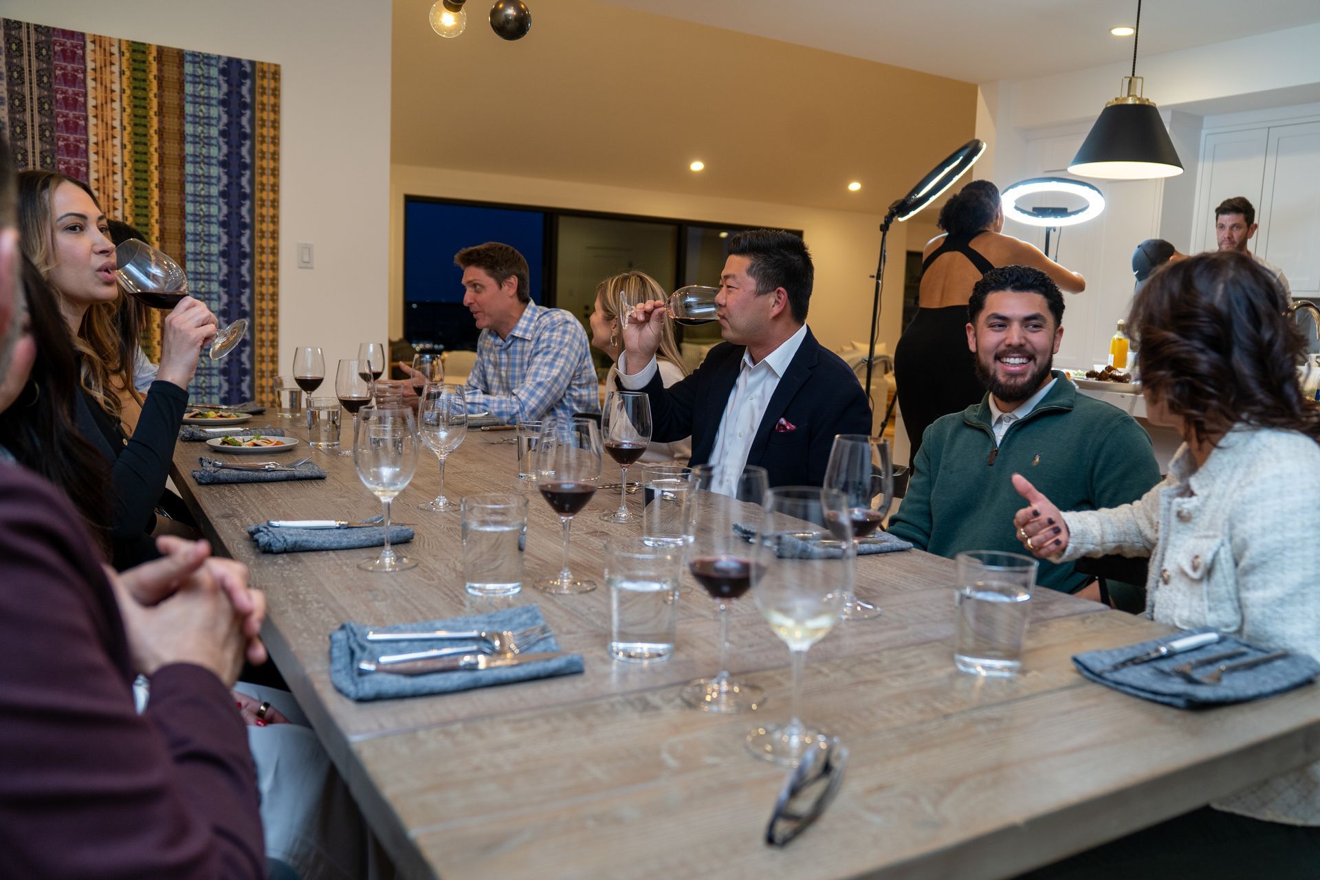 A group of people are sitting at a long table drinking wine.
