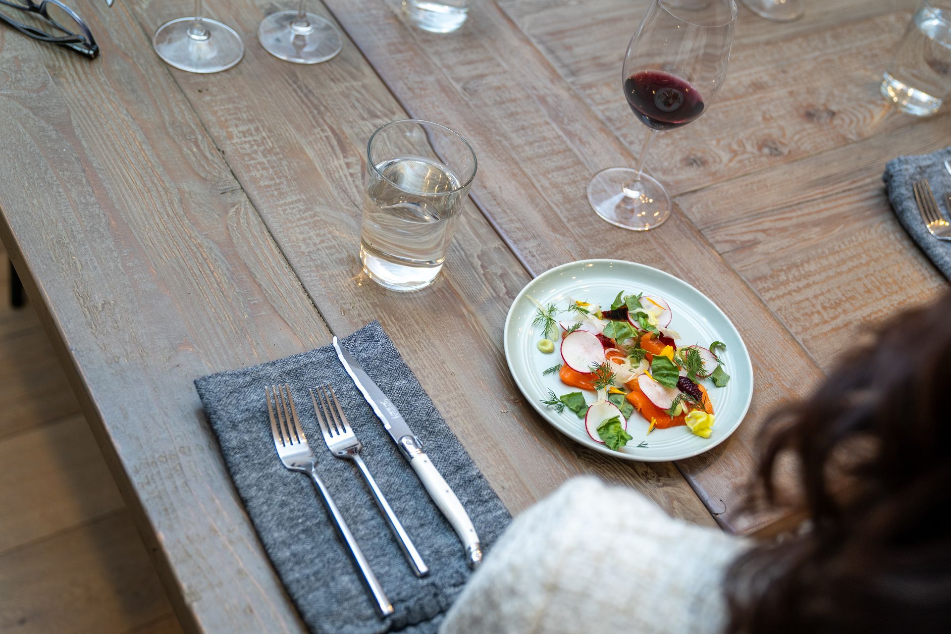 A woman is sitting at a table with a plate of food and glasses of wine.