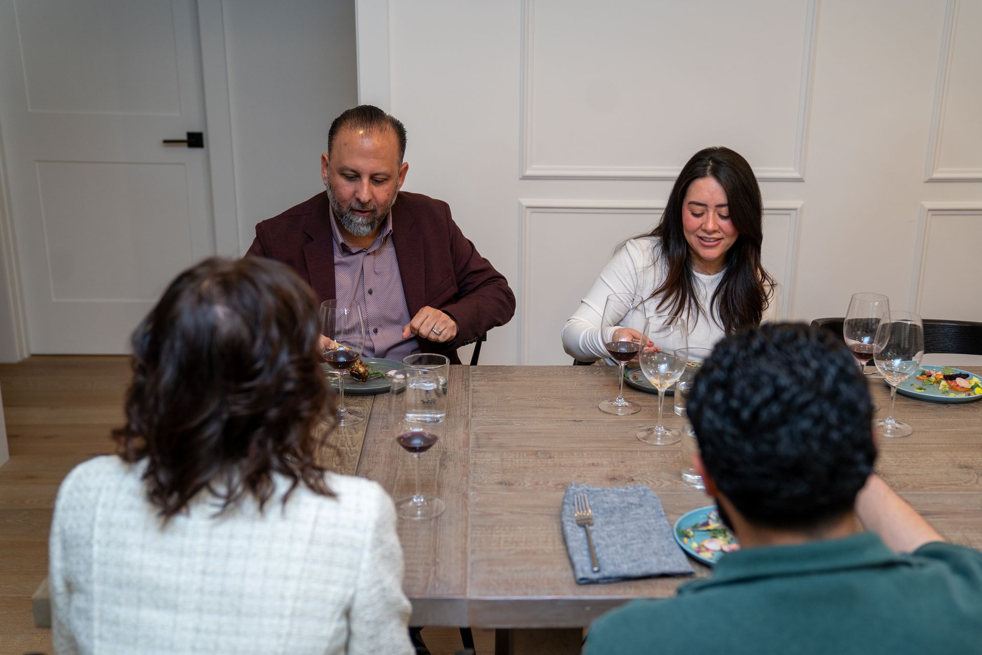 A group of people are sitting at a table eating and drinking wine.