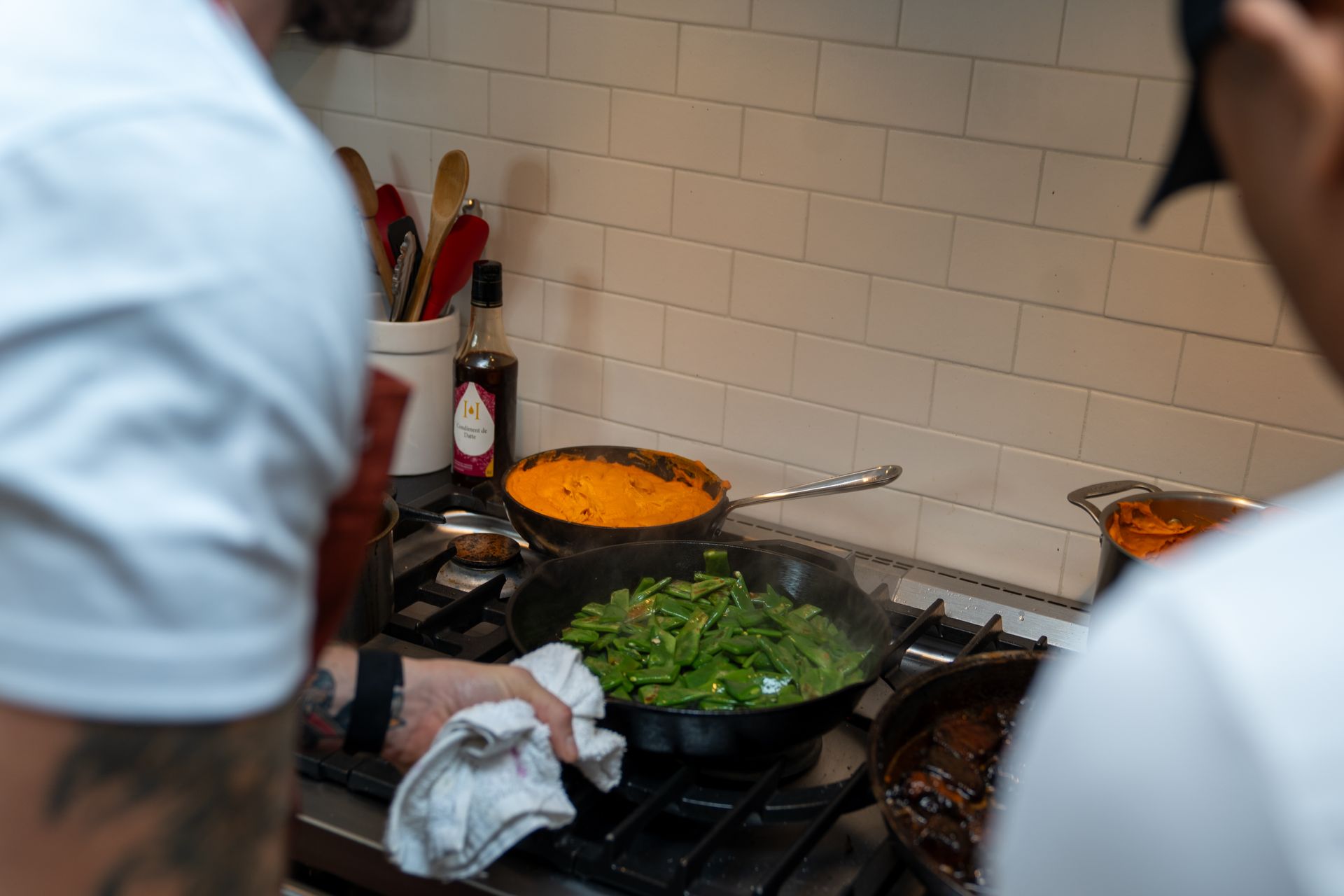 Two men are cooking food on a stove in a kitchen.