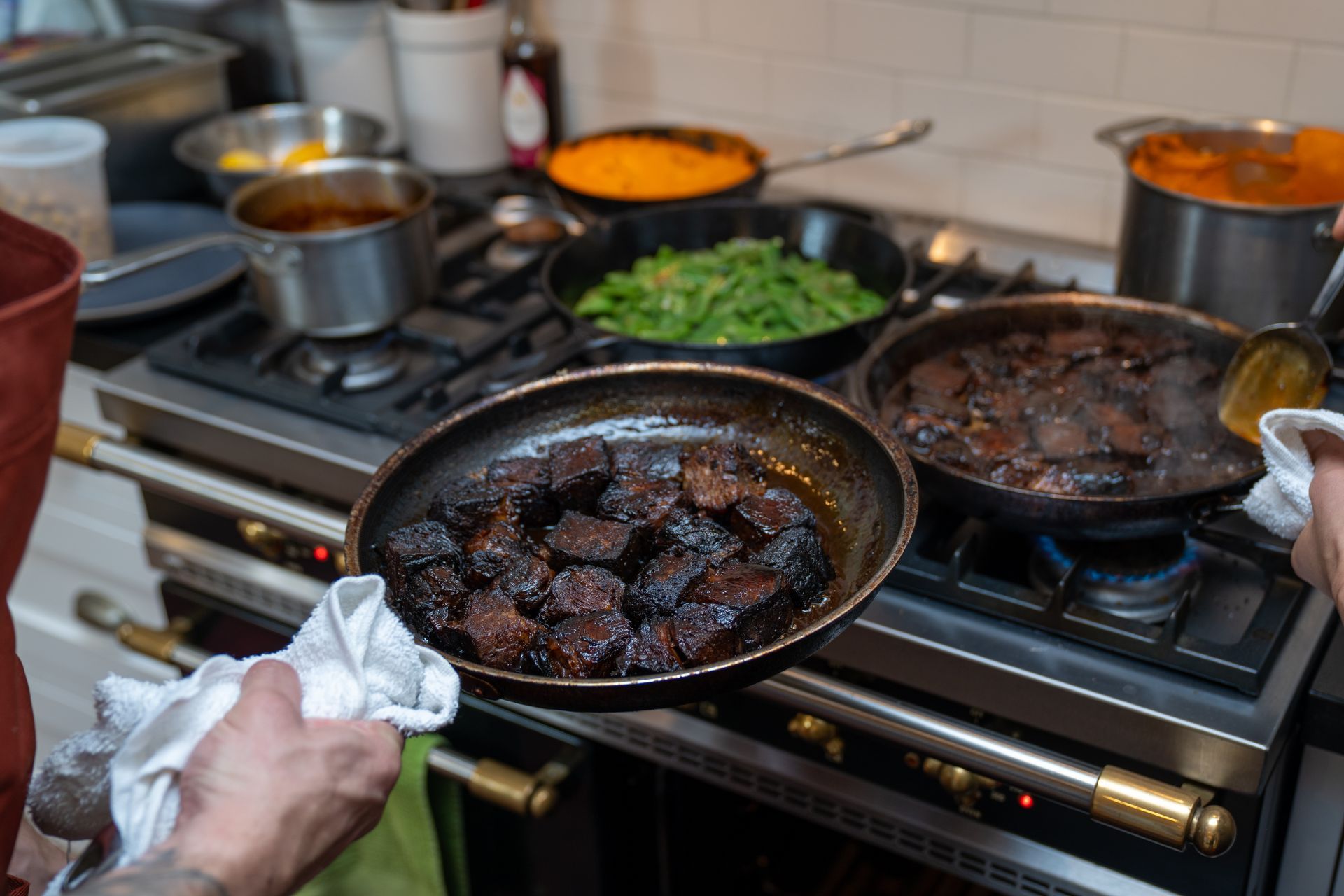 A person is holding a pan of food in front of a stove.
