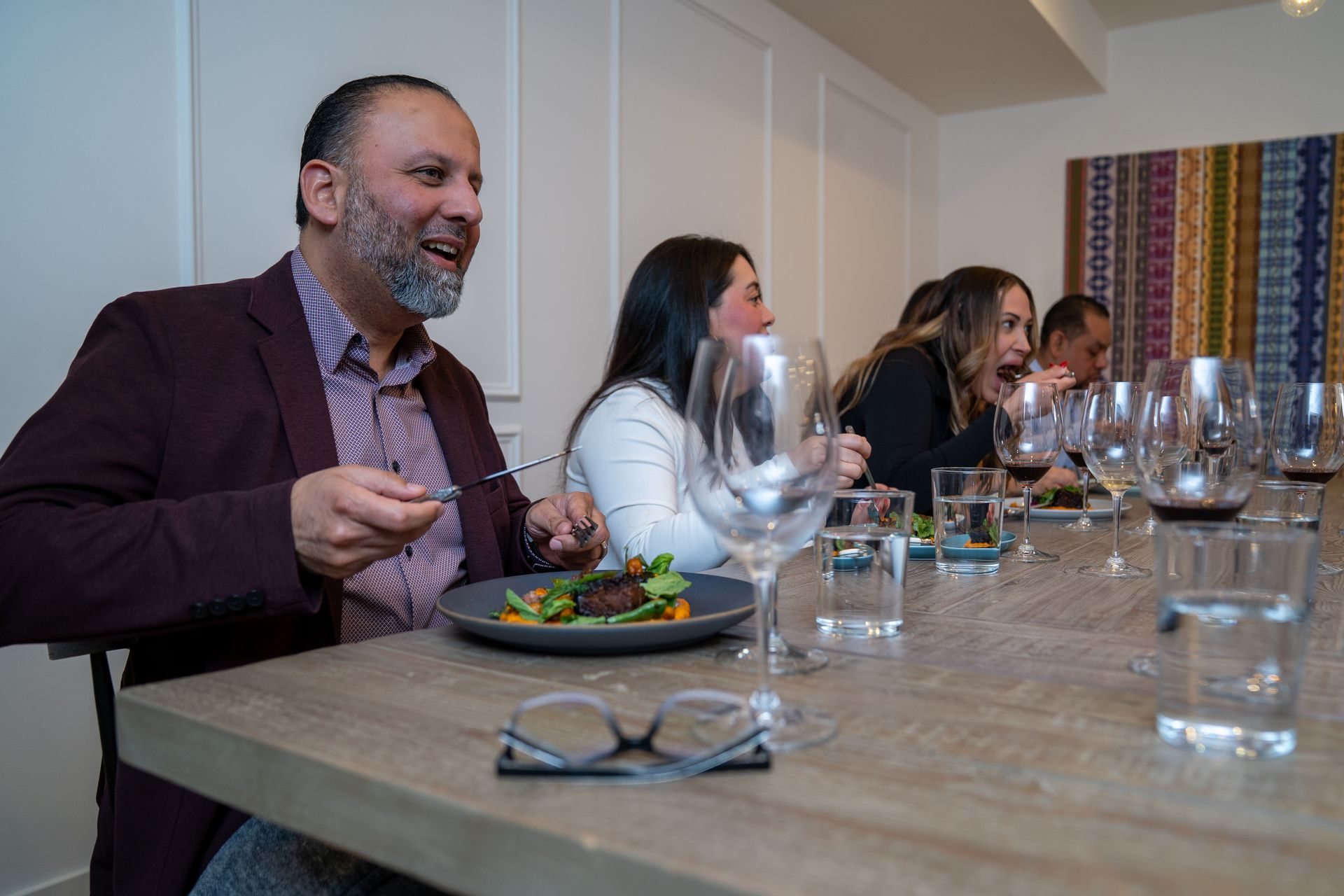 A group of people are sitting at a table eating food and drinking wine.