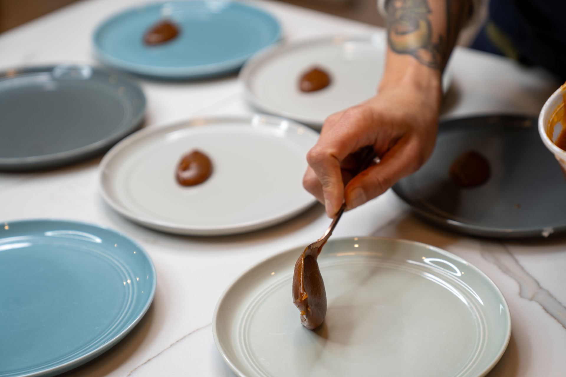 A person is spreading sauce on a plate with a spoon.