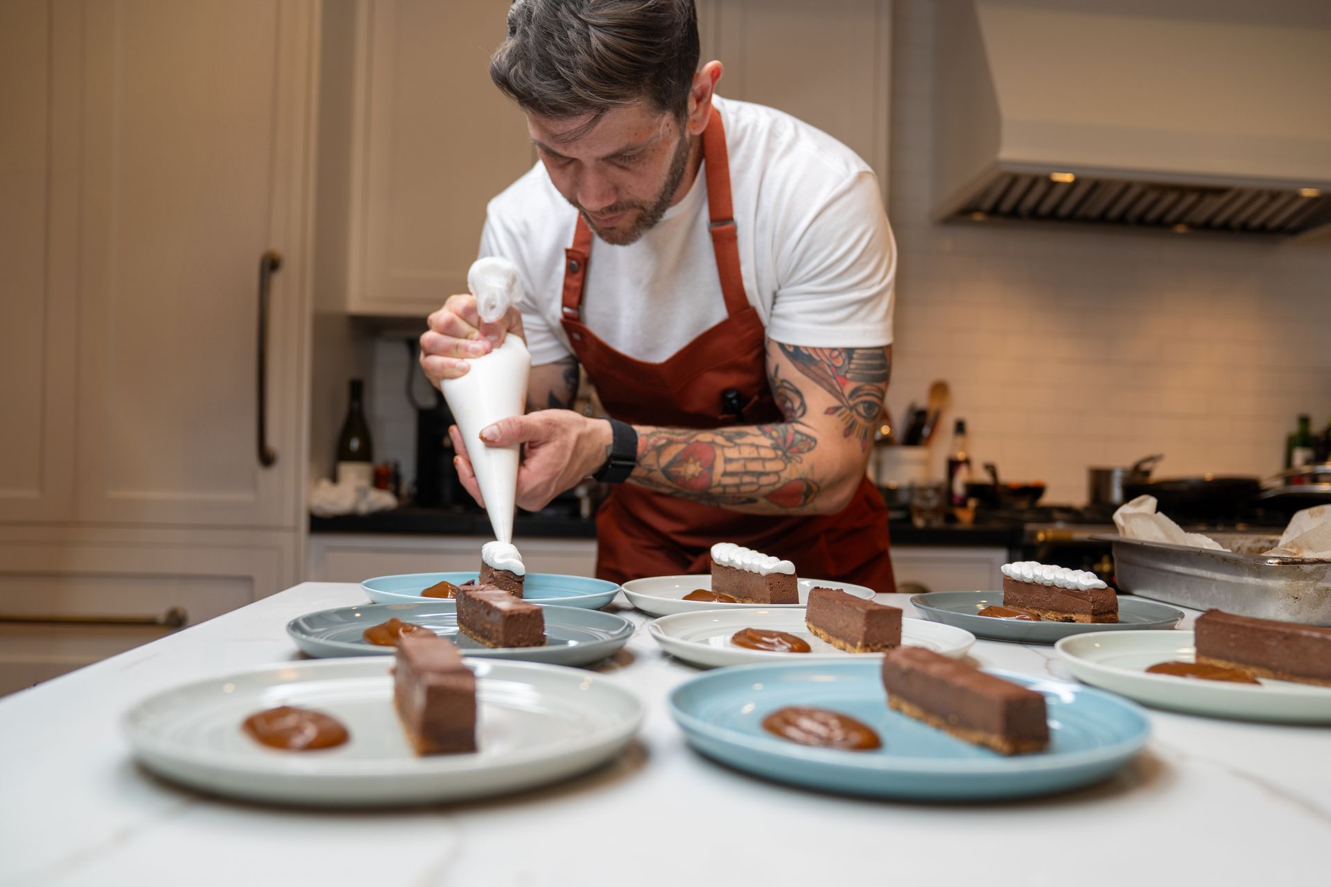 A man is decorating desserts on plates in a kitchen.