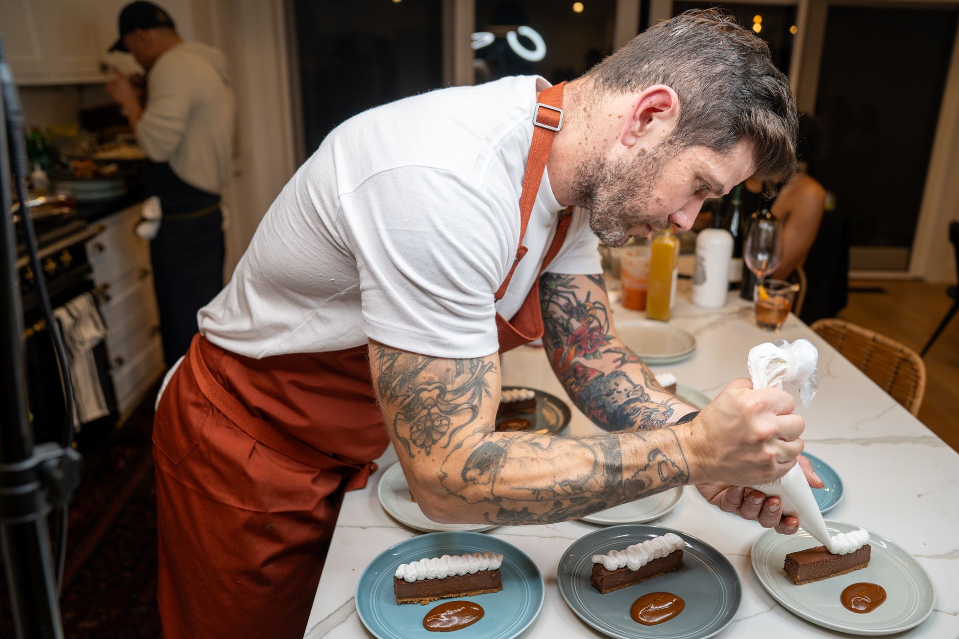 A man in an apron is decorating a dessert on a table.