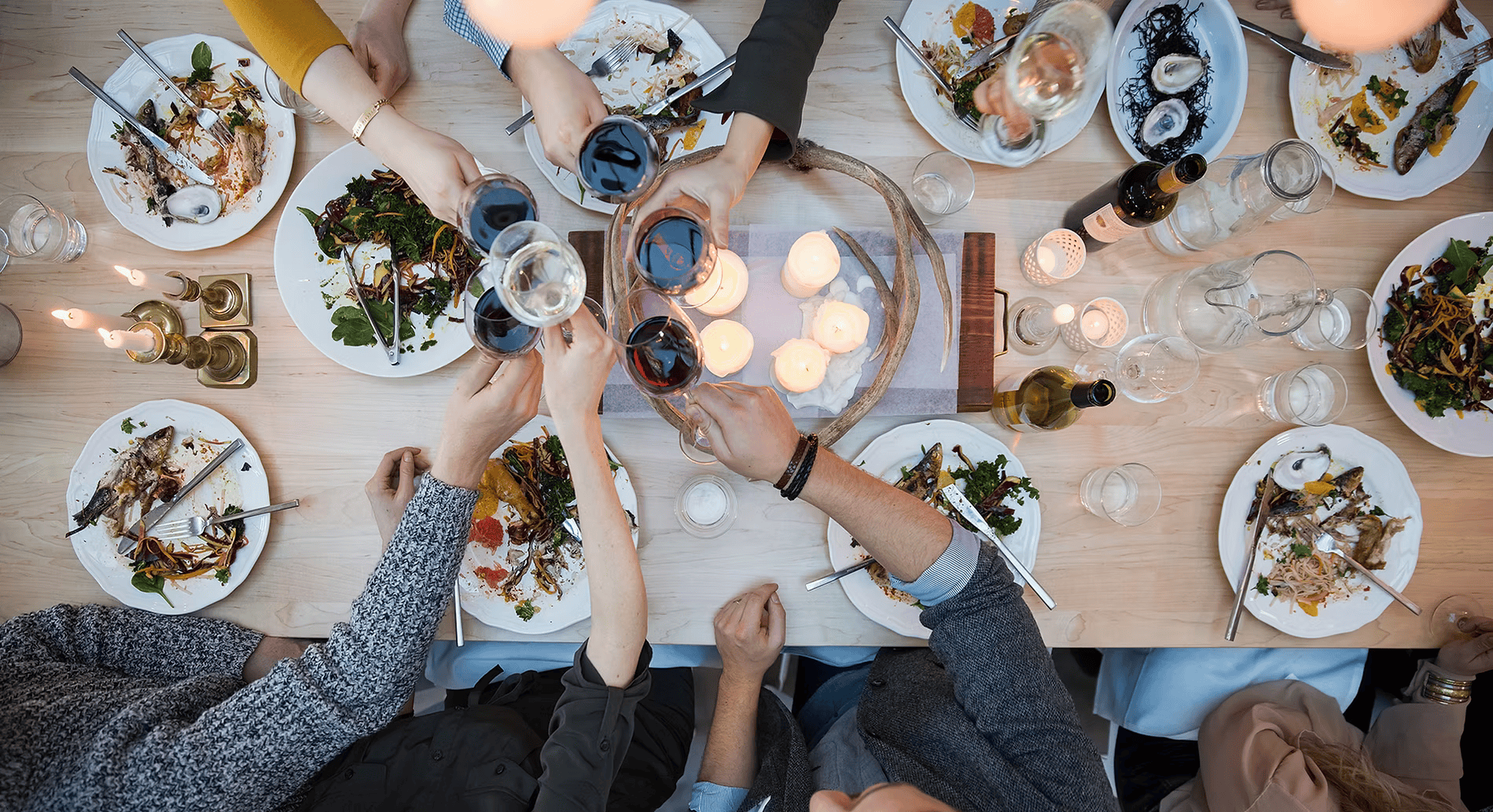 A group of people are sitting around a table with plates of food and glasses of wine.