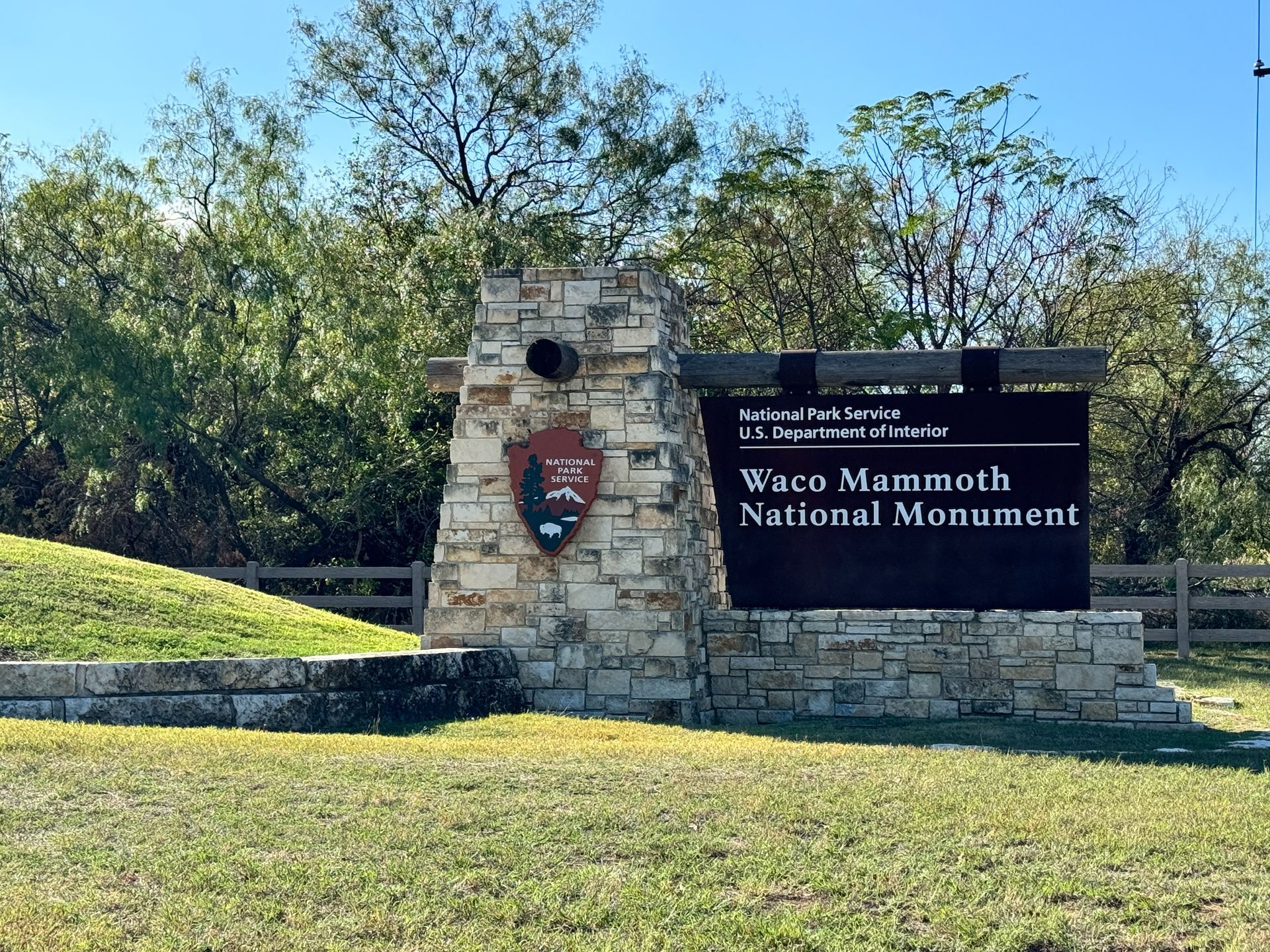 A sign for a national monument is sitting in the middle of a grassy field.
