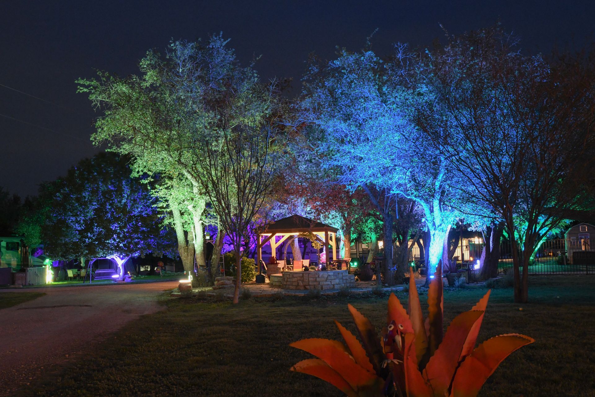 A gazebo is lit up with colorful lights in a park at night.