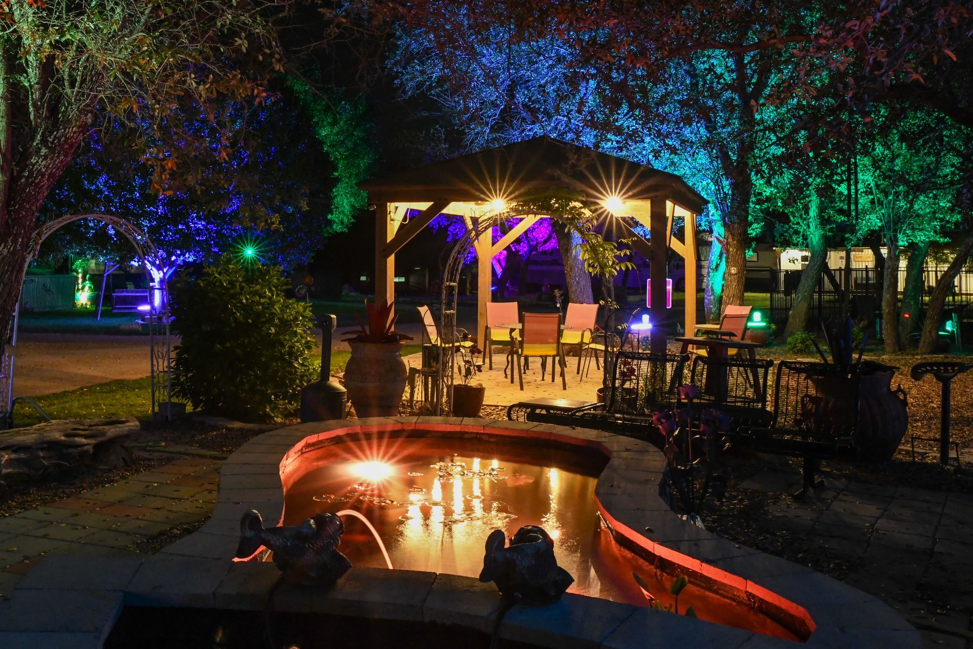A gazebo with a fountain in front of it is lit up at night.