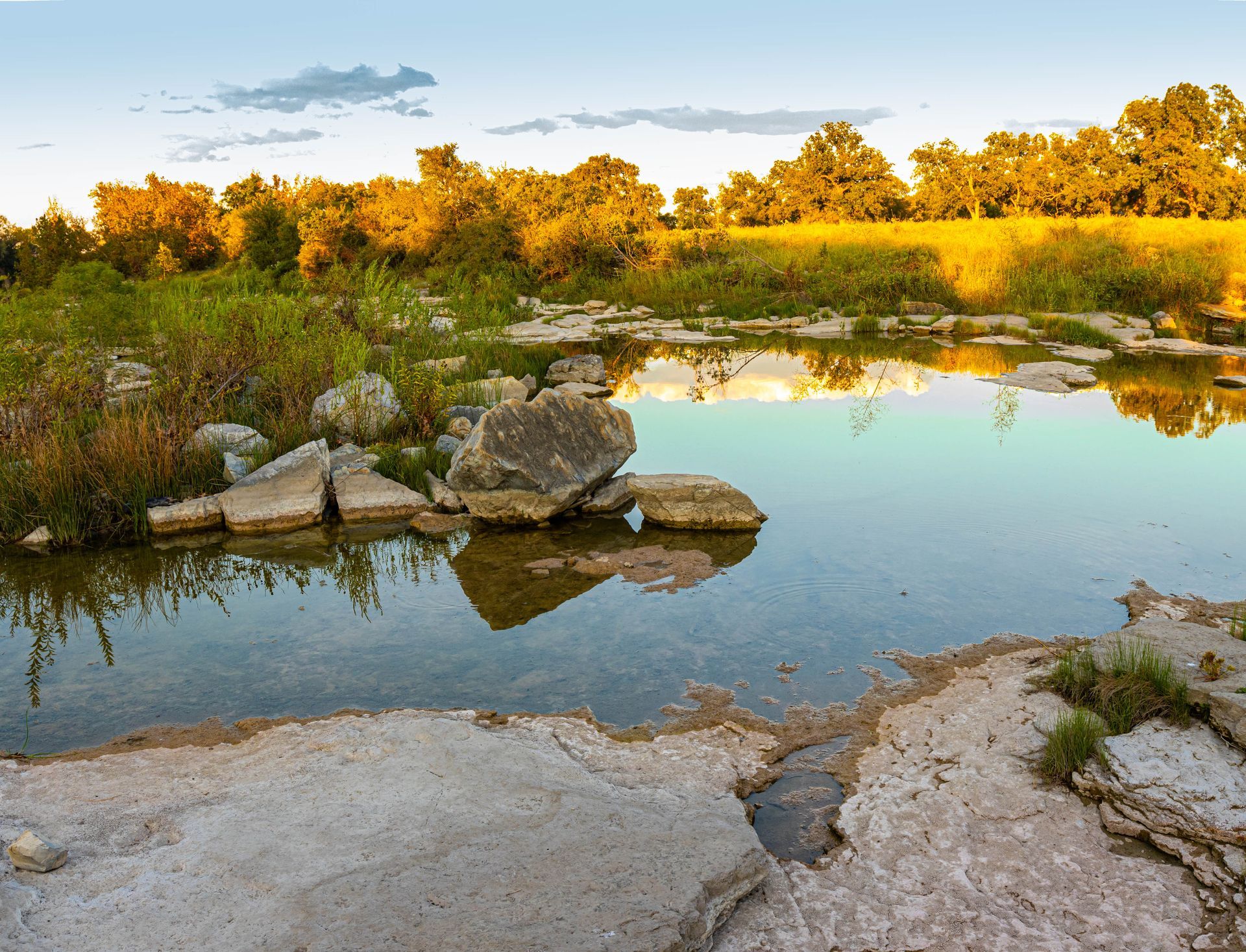 A river surrounded by rocks and grass with trees in the background
