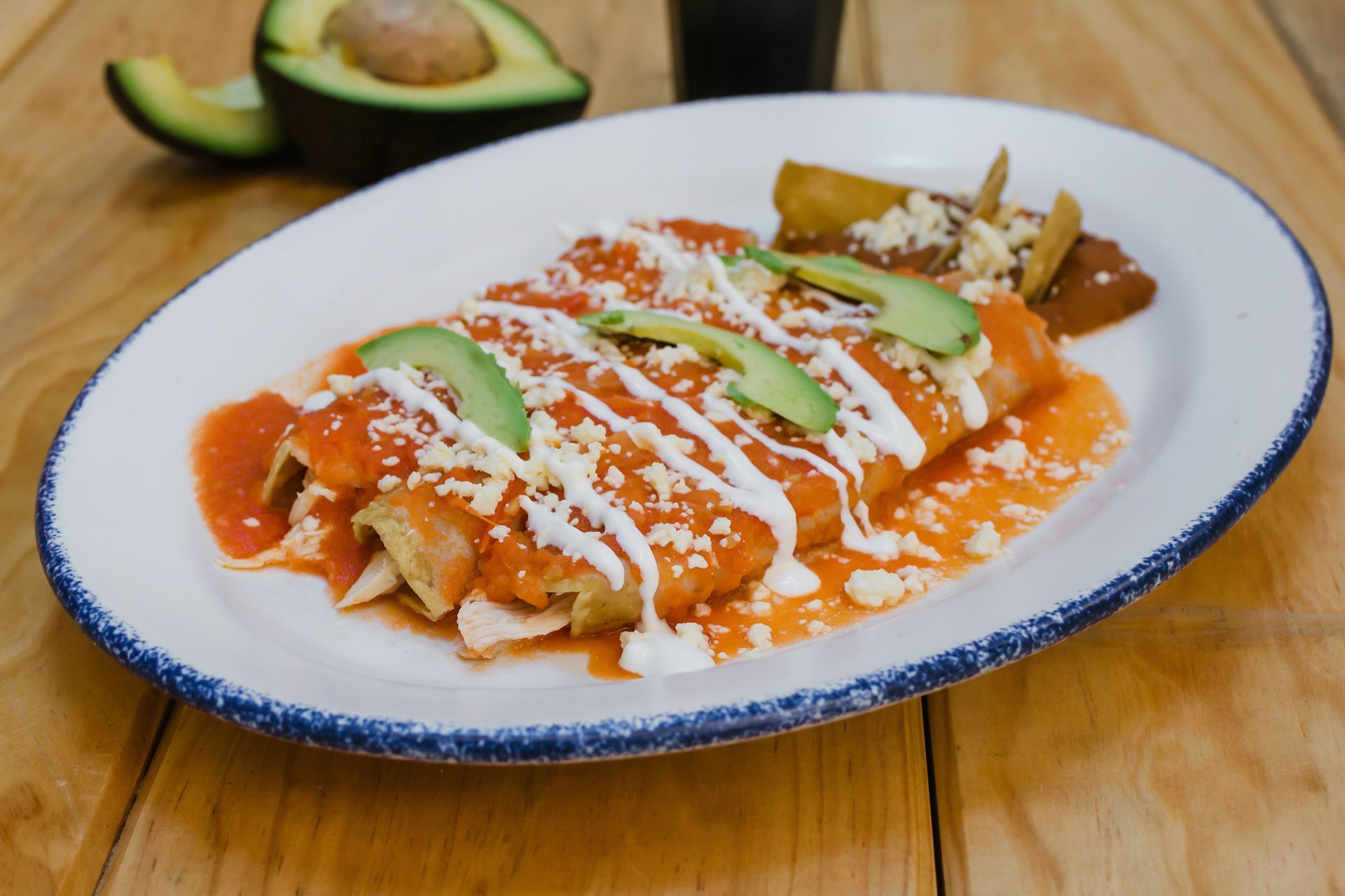 A white plate topped with enchiladas and avocado on a wooden table.