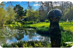 There is a statue in the middle of a park next to a pond.
