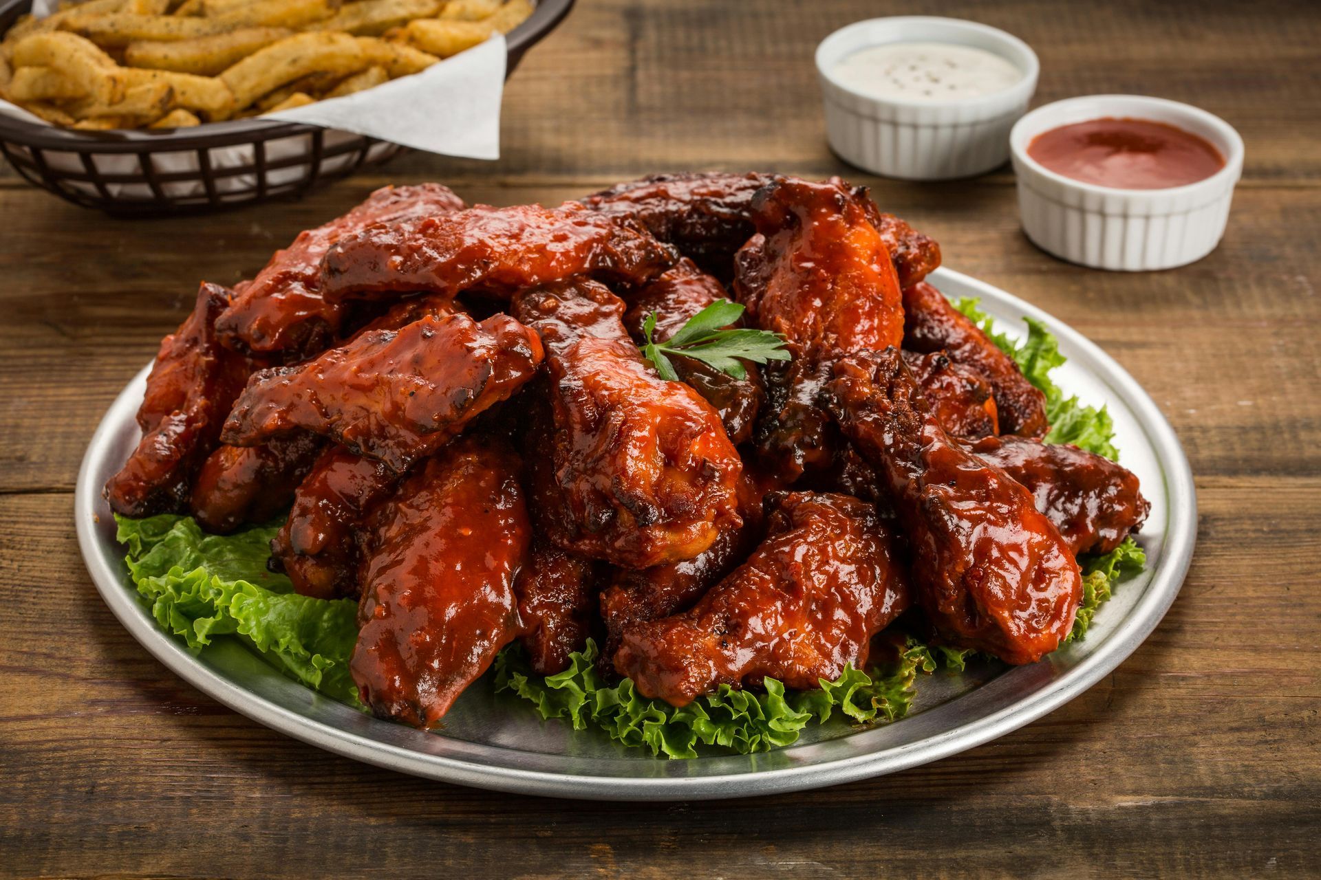 A plate of chicken wings and french fries on a wooden table.