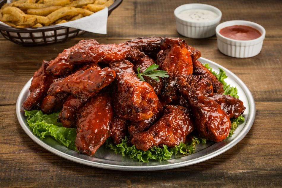 A plate of chicken wings and french fries on a wooden table.