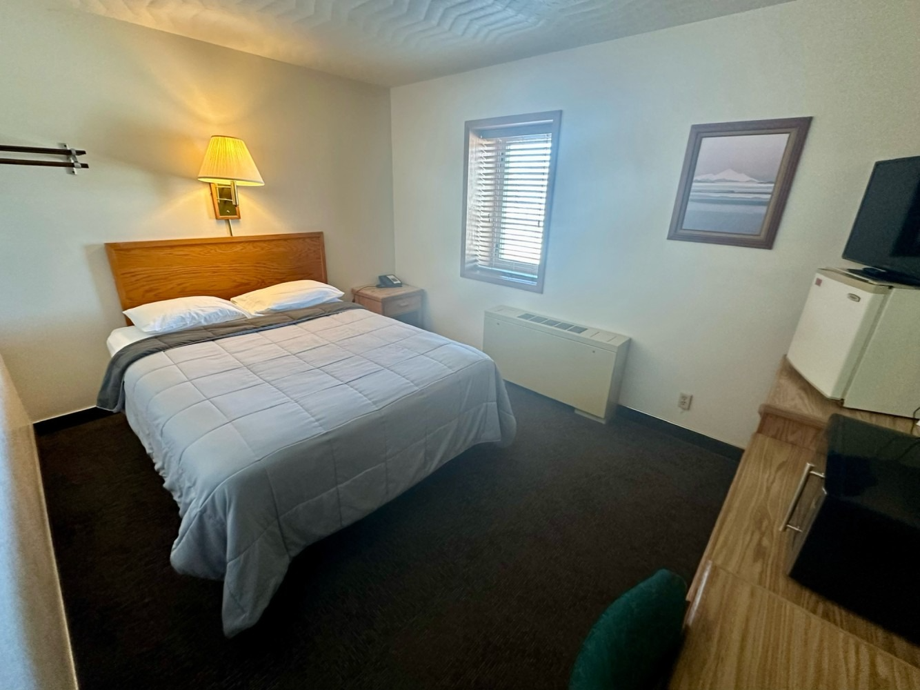 Small motel room with a bed, desk, TV, and a window.