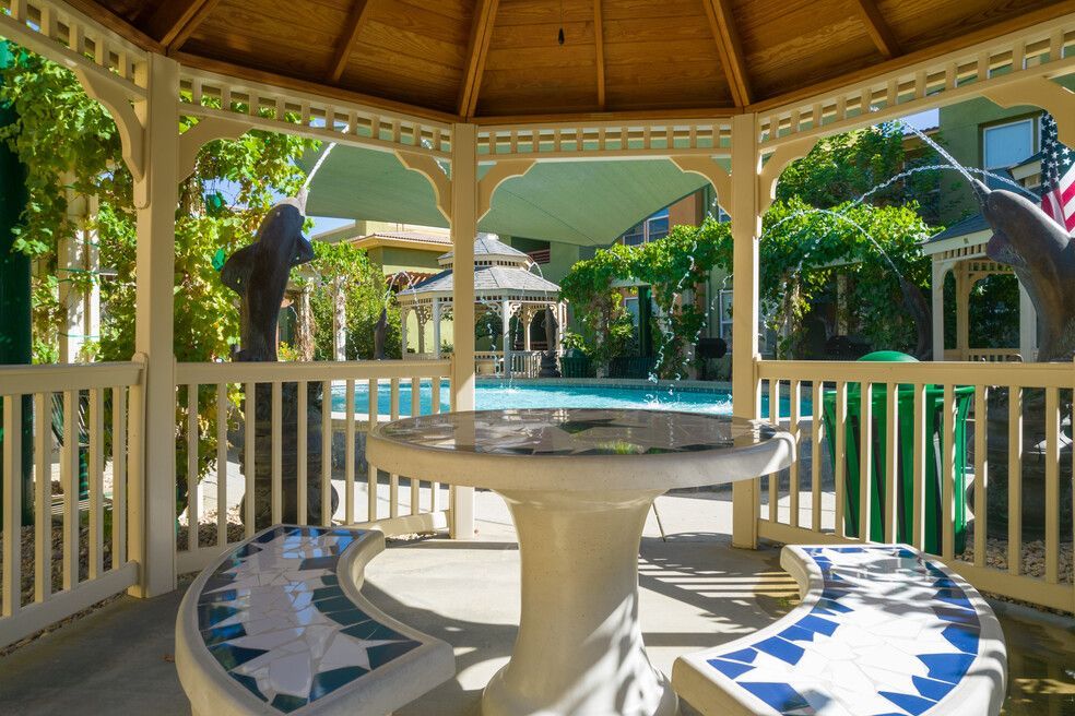 A gazebo with a table and benches in front of a pool.