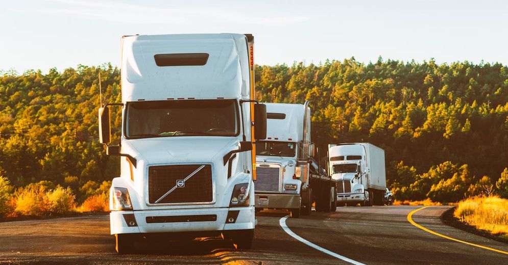 A row of semi trucks are driving down a curvy highway.