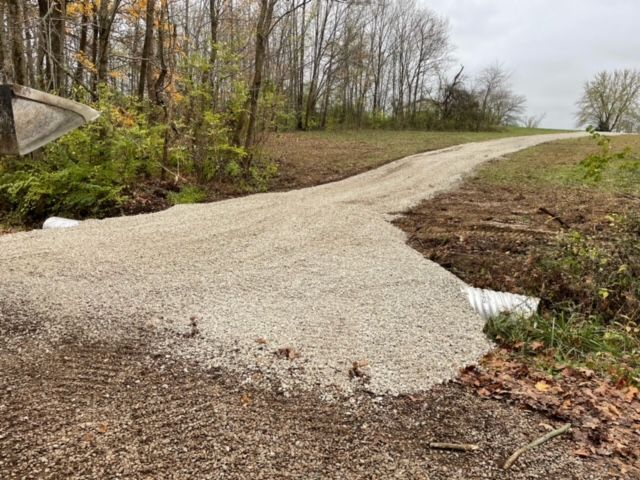 A yellow and green tractor is plowing a dirt road.