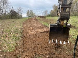 A yellow and green tractor is plowing a dirt road.