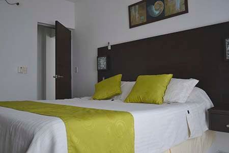Cama bien hecha con sábanas blancas, camino de mesa y almohadas de color verde lima en un dormitorio moderno.
