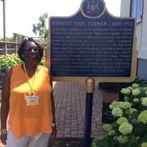 Woman in orange shirt stands by Harriet Tubman historical marker.