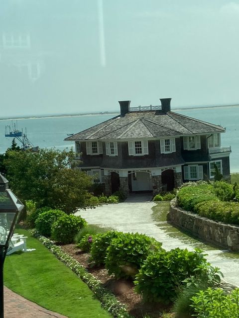 Coastal house with shingled roof, driveway, and ocean view on a sunny day.