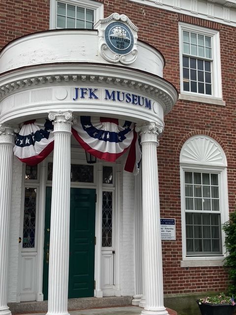 Exterior view of the JFK Museum building with white columns, a green door, and red, white, and blue bunting.
