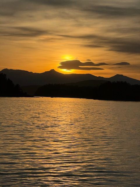 Golden sunset over a lake, silhouetting mountains and reflecting light on the water.