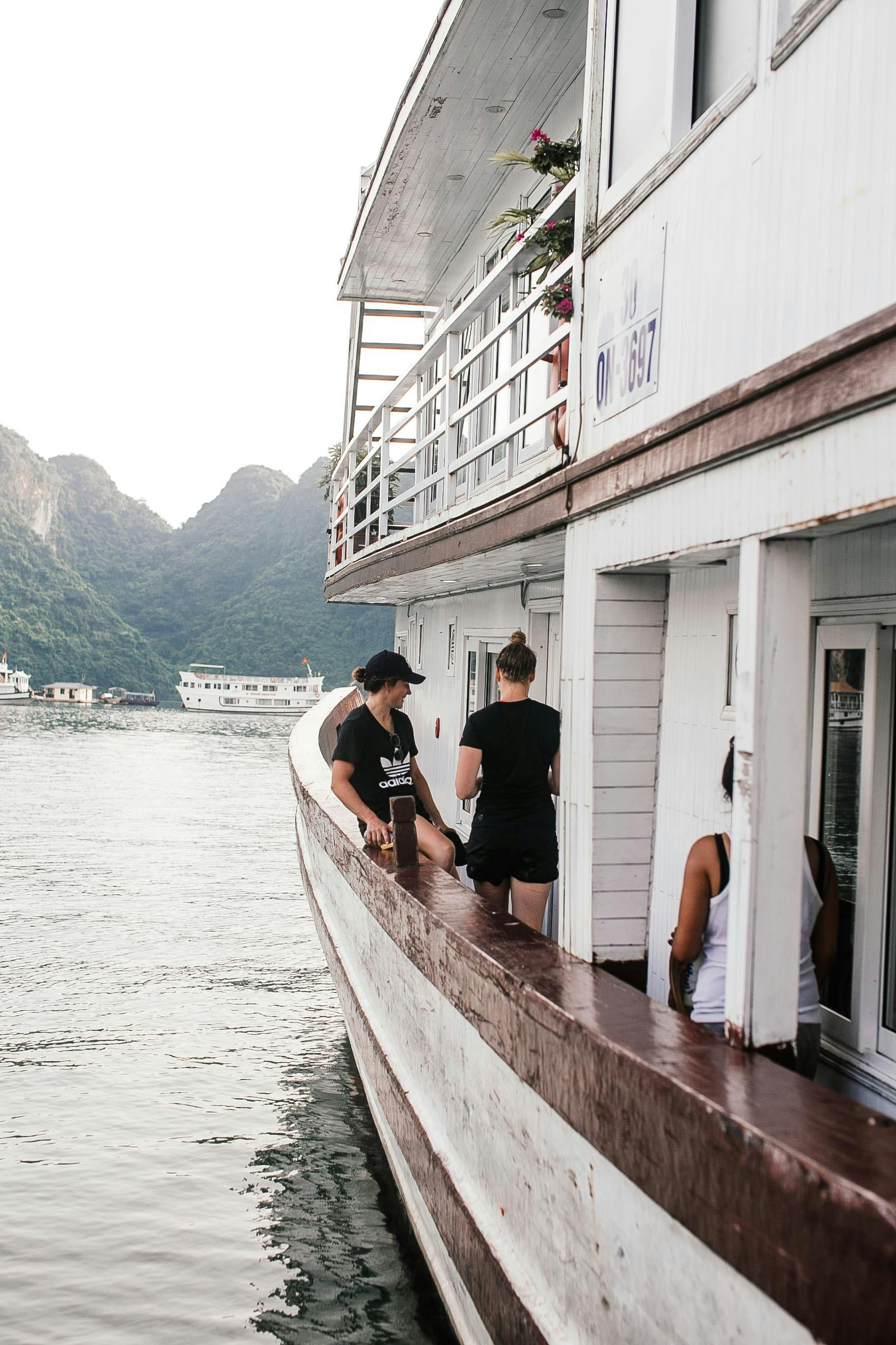 Hiker with blue backpack hikes along a river toward snow-capped mountains. Green foliage lines the path.