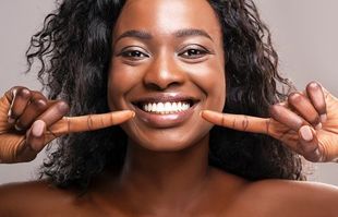 Woman smiling pointing to mouth after visiting our restorative dentist in Topeka KS