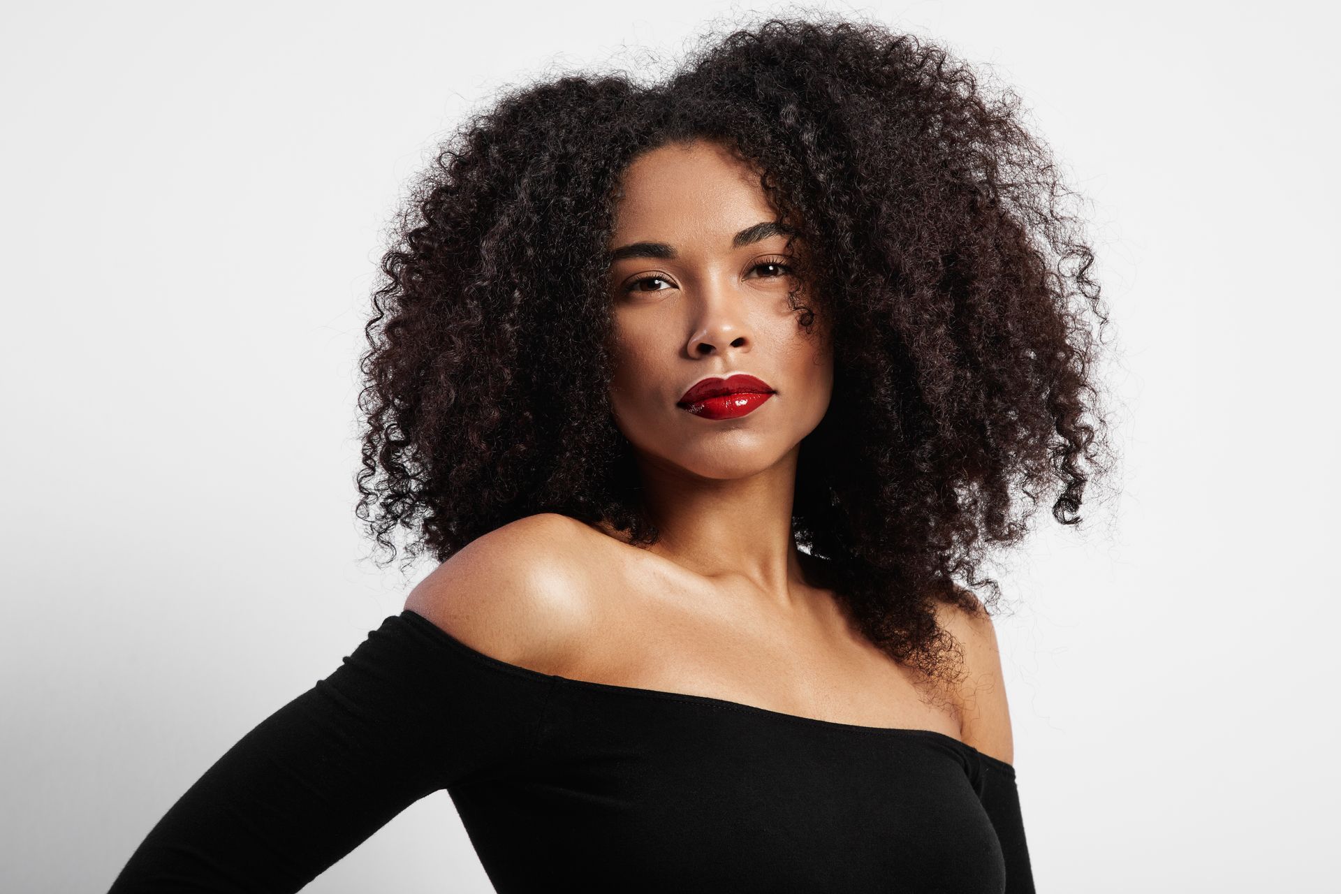a woman with curly hair and red lipstick is wearing a black off the shoulder top