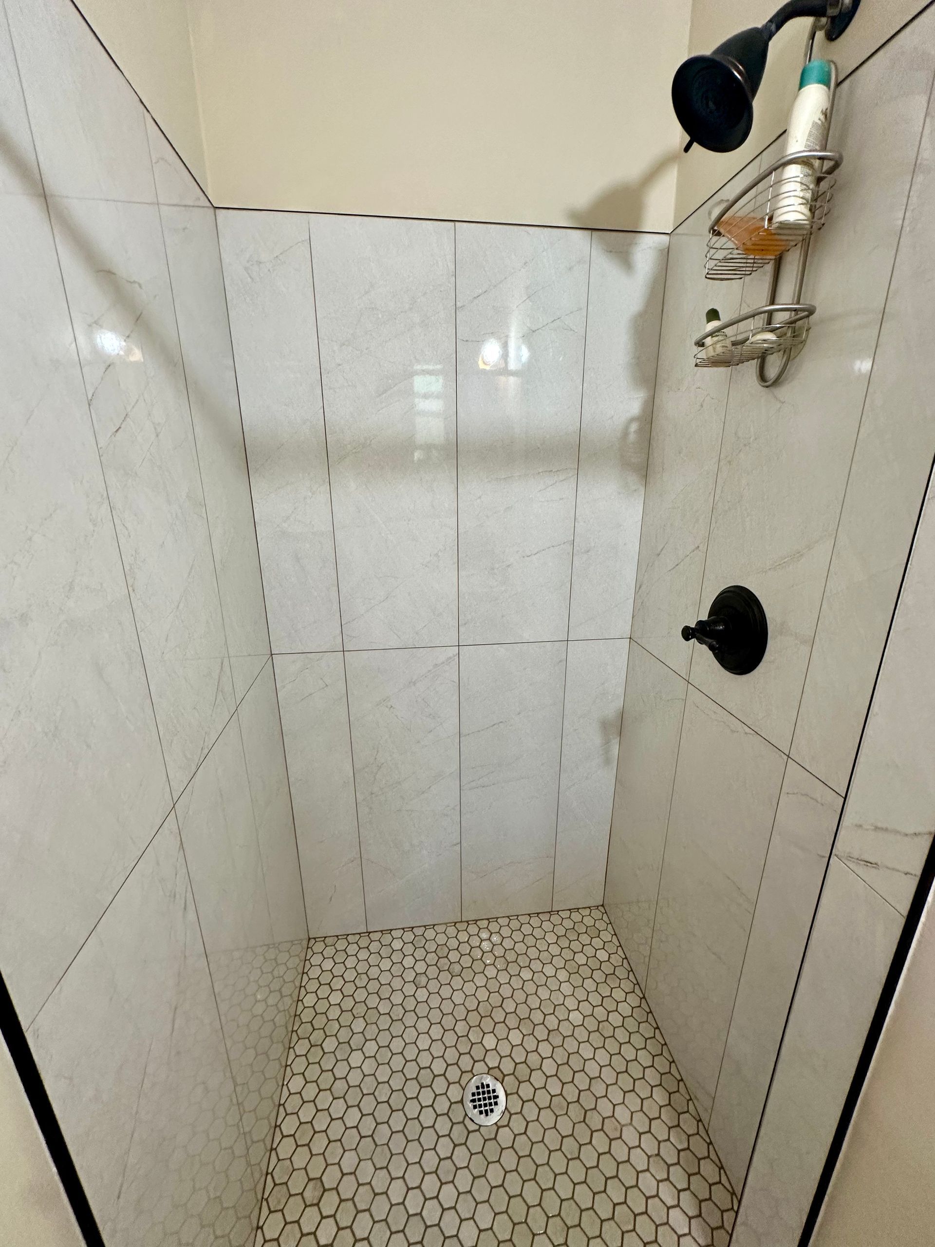 A shower with white tiles and a black shower head