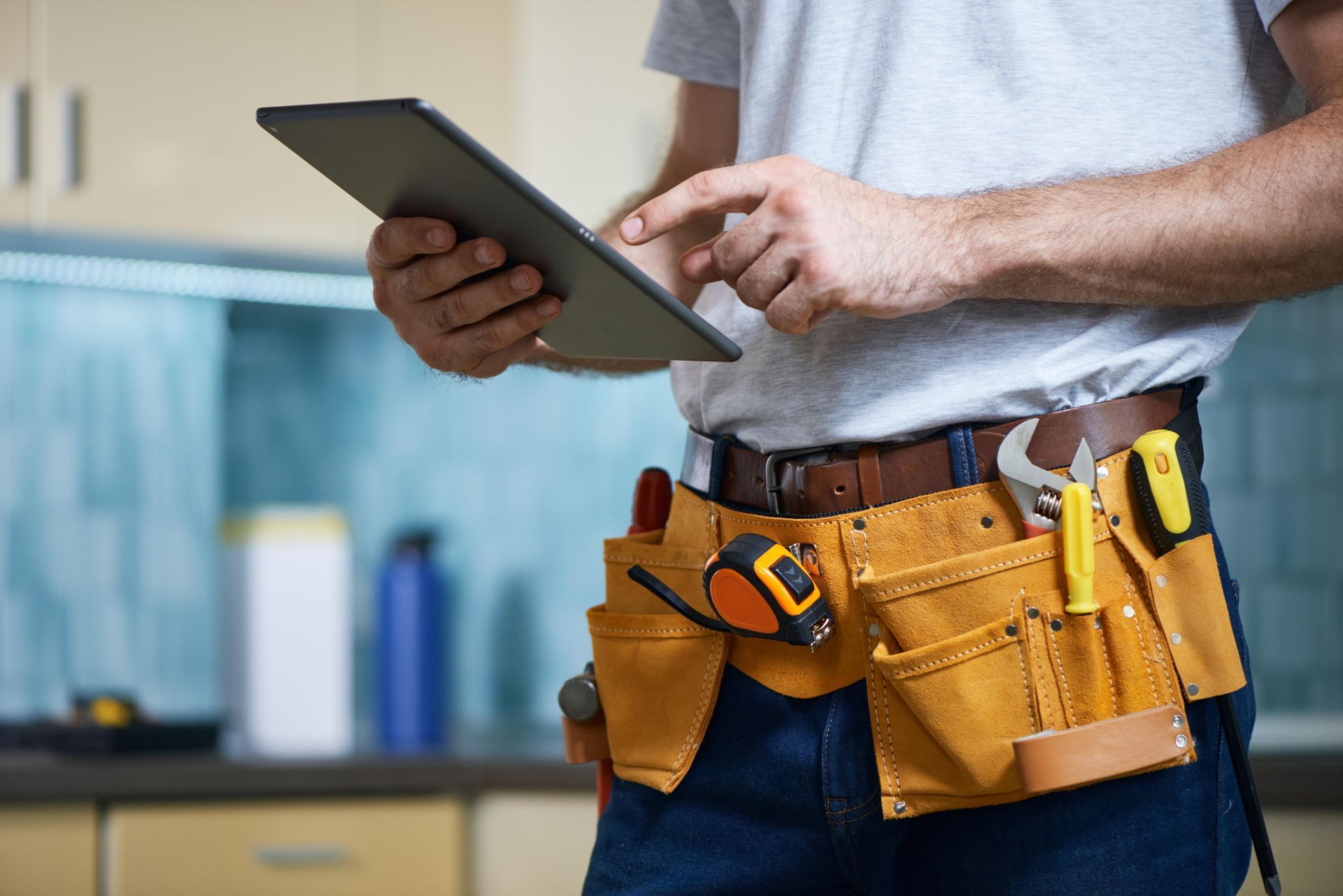 A man wearing a tool belt is using a tablet computer.