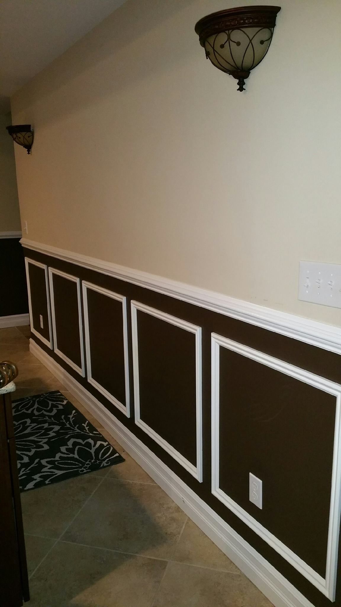 A hallway with brown and white trim and a lamp on the wall.