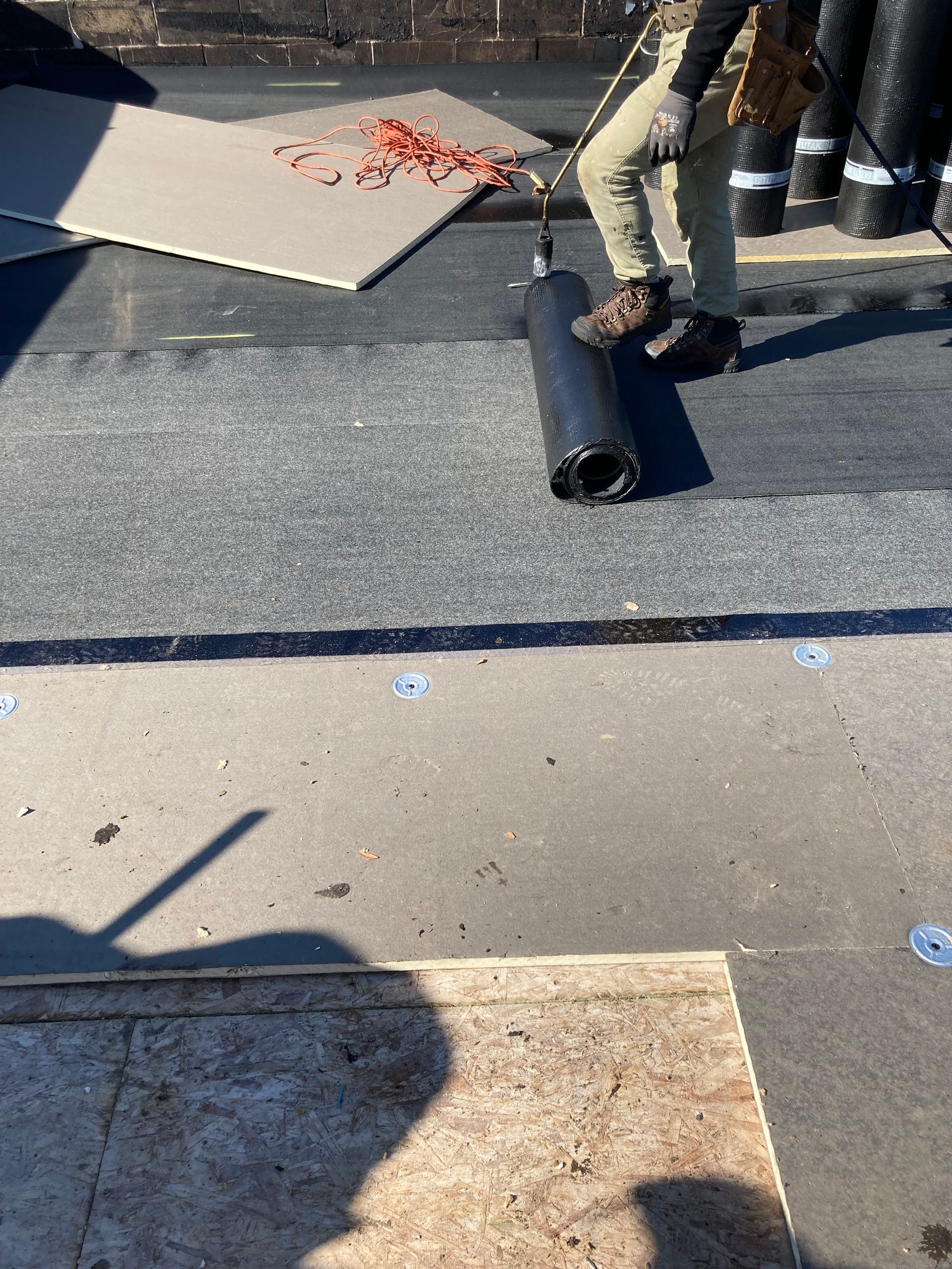 Roofer rolling out a black roofing membrane on a flat roof.