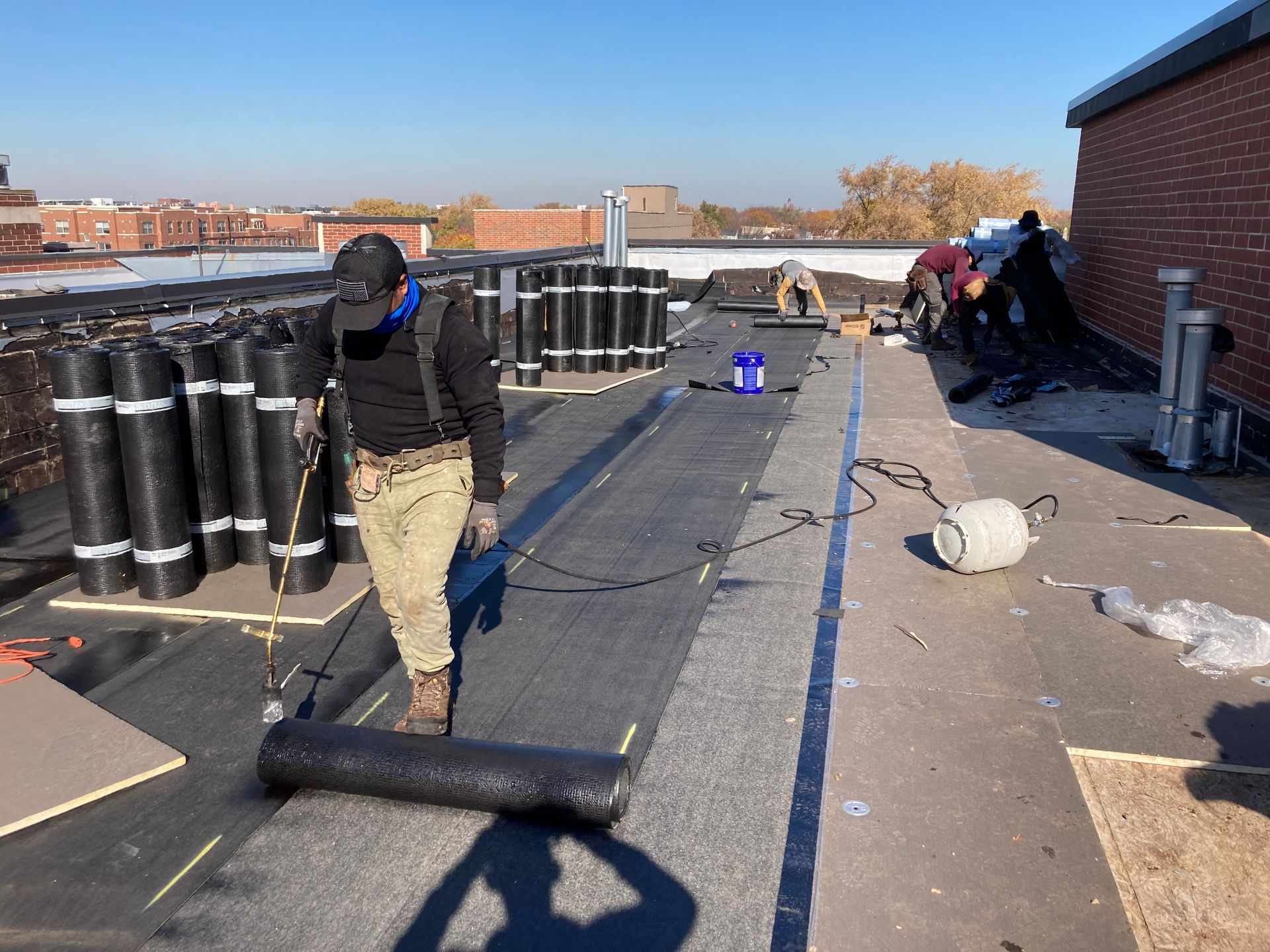 Roofers installing a new flat roof on a building. They are rolling out roofing material on a sunny day.