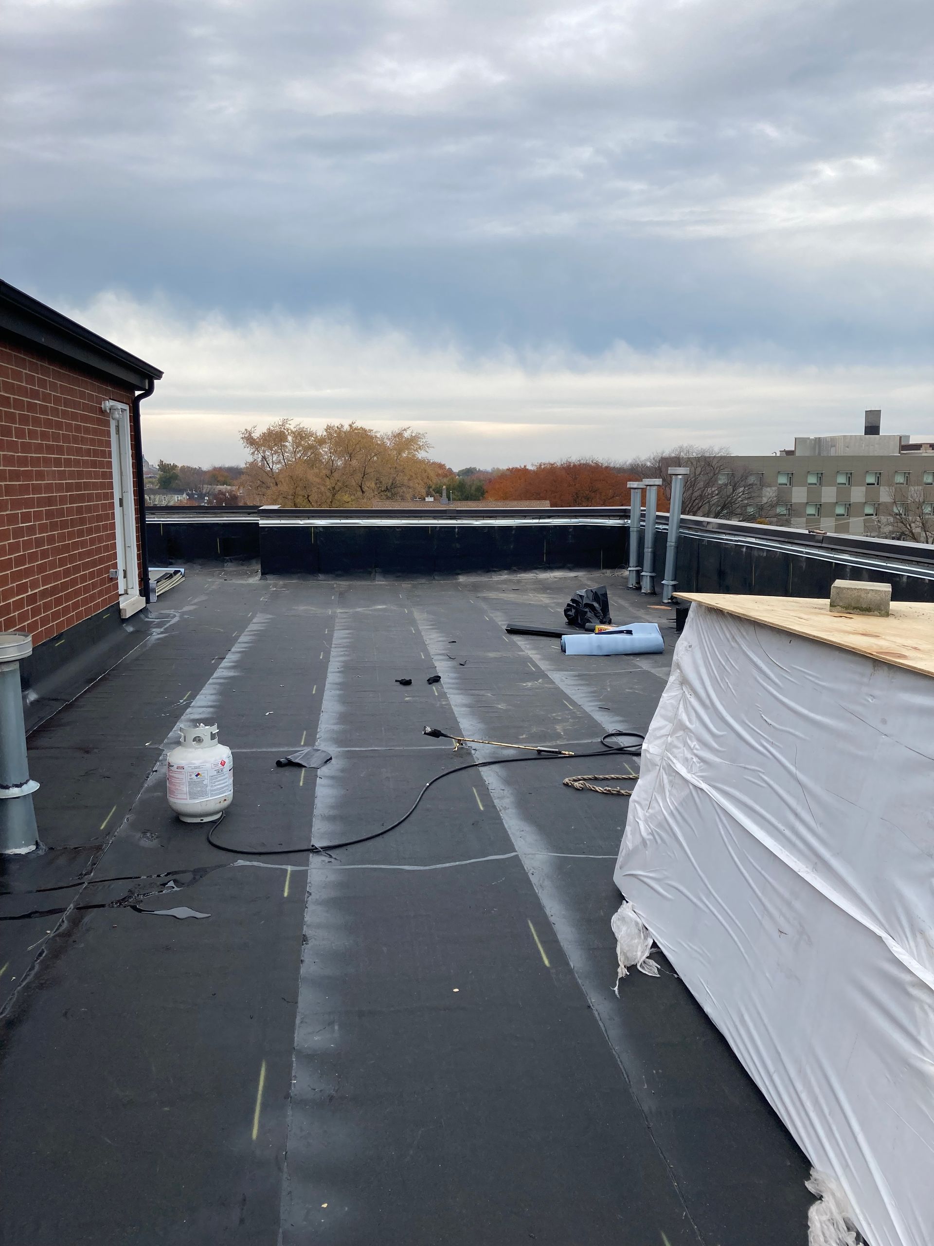 Flat roof with black surface, propane tank, and overcast sky. Building exterior, construction site.