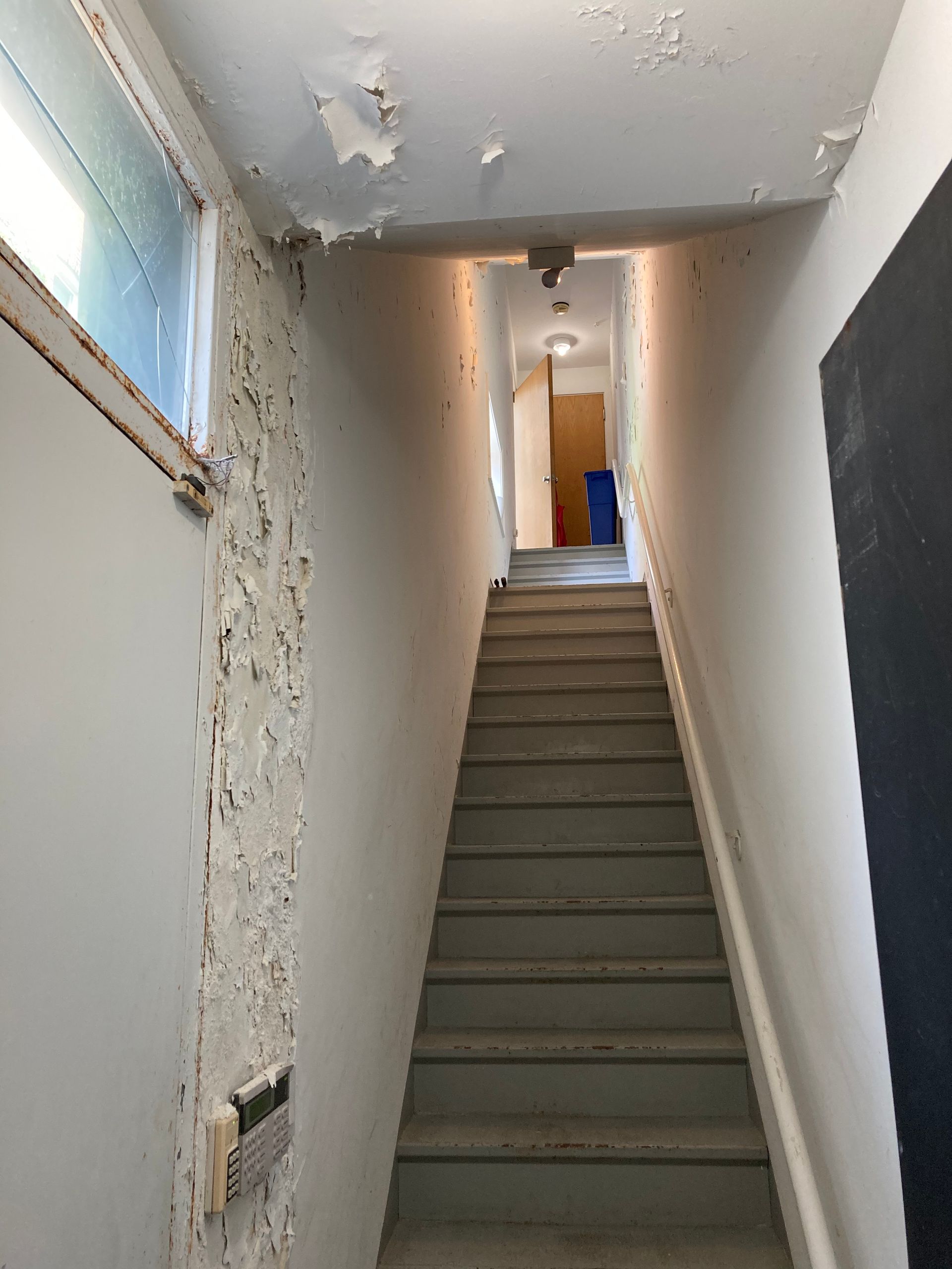 Narrow staircase leading to a doorway. Peeling paint on wall, window on the left.