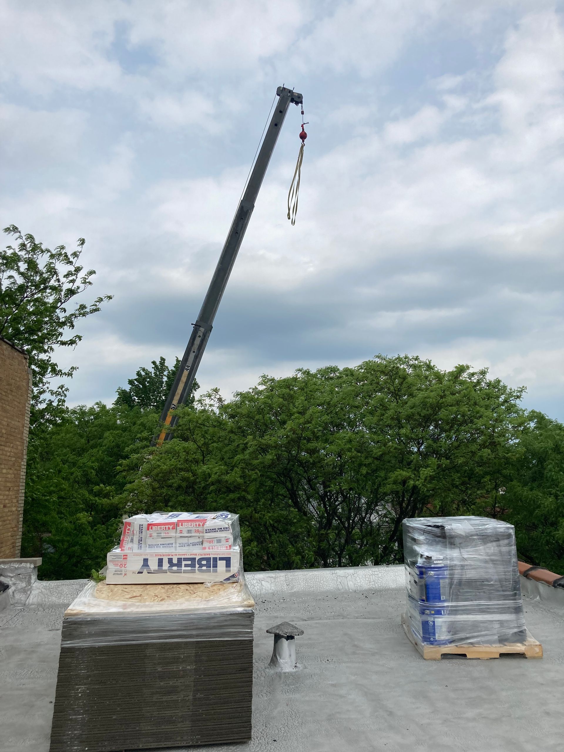 A crane lifting building materials on a flat roof, cloudy sky background.