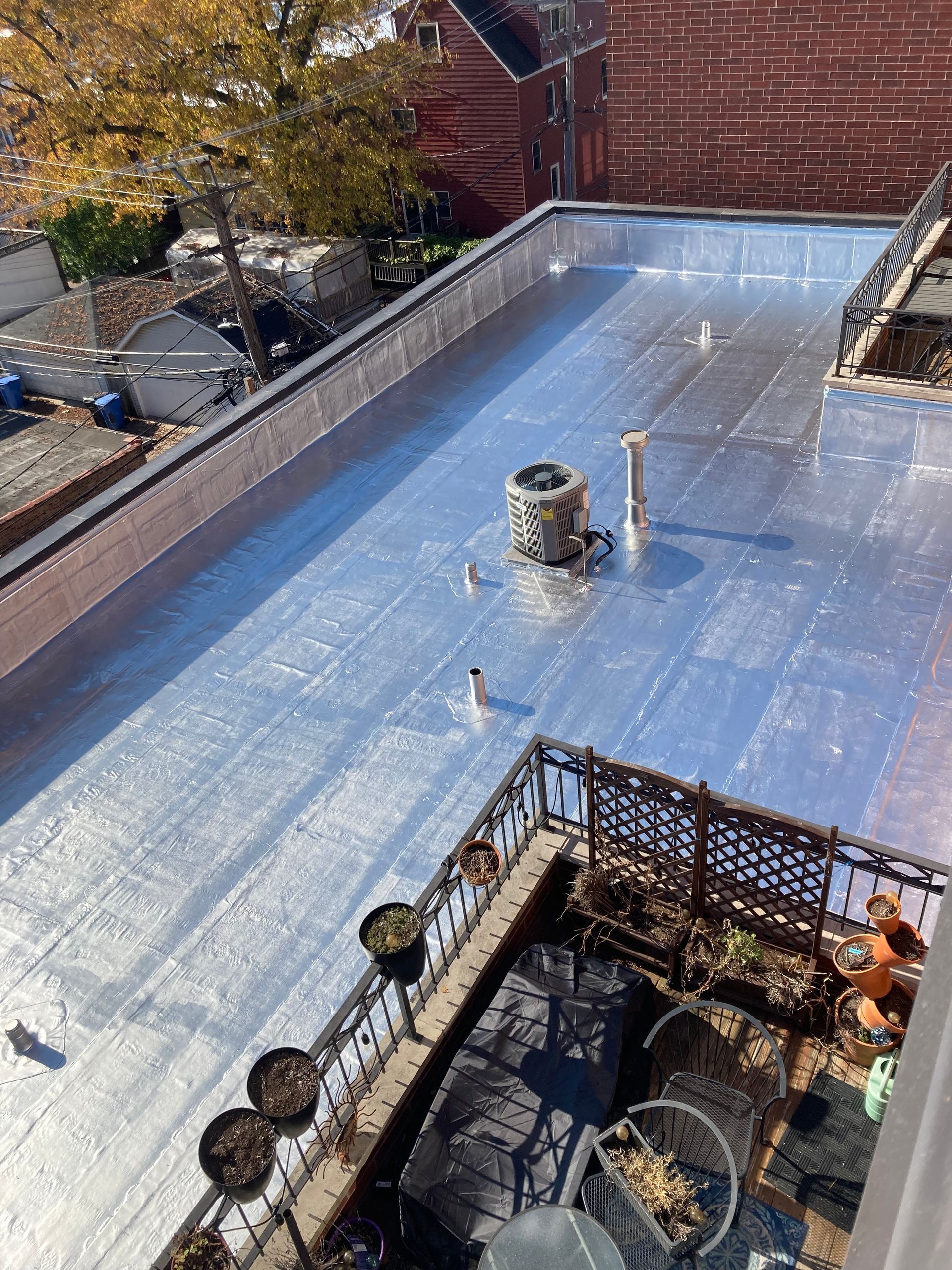 View of a flat rooftop with reflective material, surrounded by brick walls and a small patio with plants.