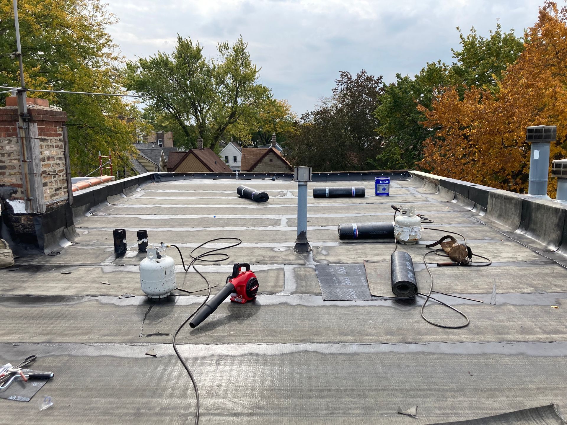 Flat roof with equipment; tools and materials scattered. Trees and sky in the background.