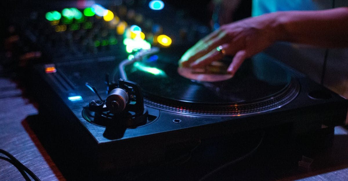 DJ spinning vinyl record on turntable with hand on disc, glowing lights in the background.