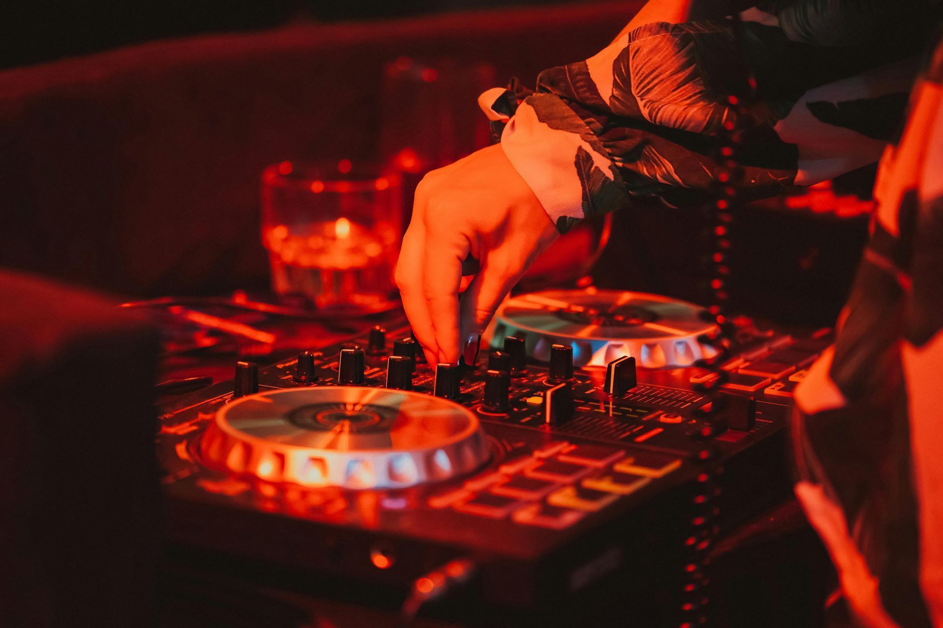 DJ at work, adjusting soundboard knobs with red lighting in a club.