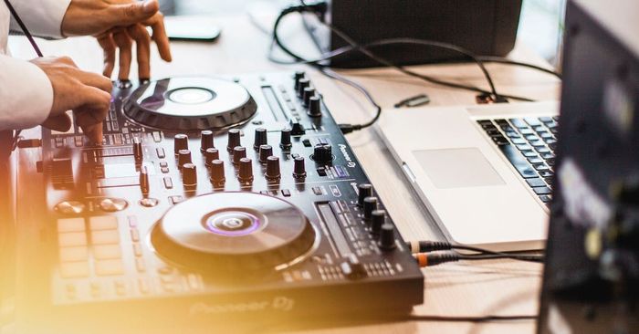 DJ using a mixer with a laptop, hands visible. Close-up shot.